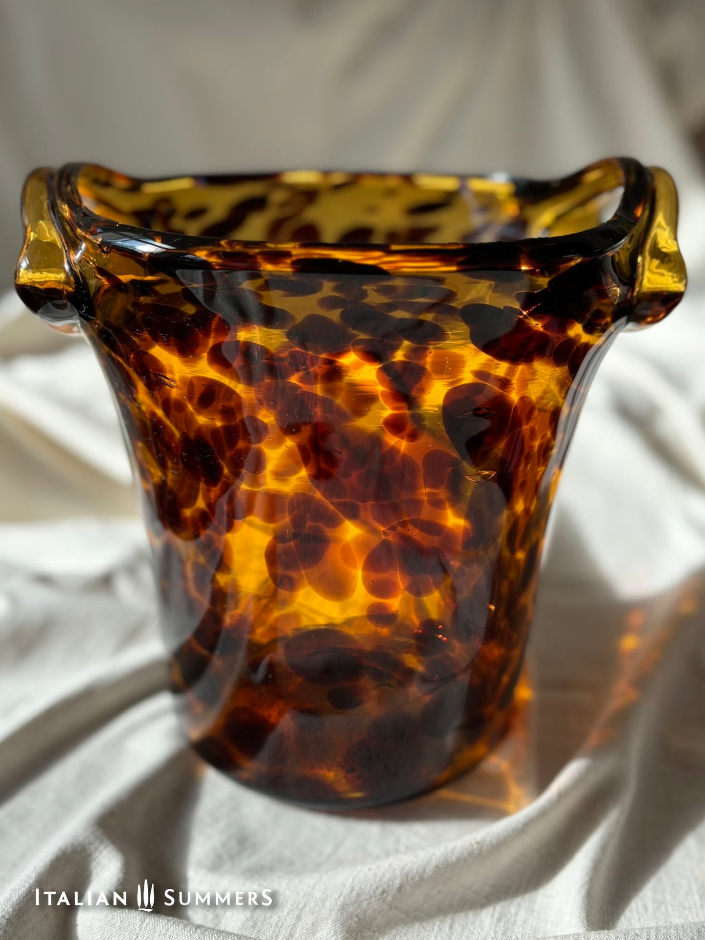 Tortoiseshell patterned glass ice bucket on a light fabric background