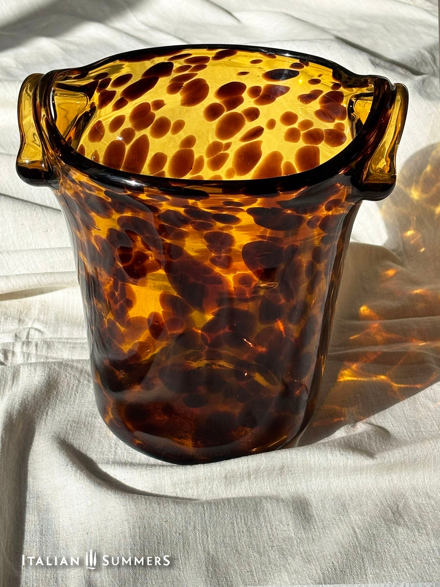 Tortoiseshell patterned glass ice bucket on a light fabric background