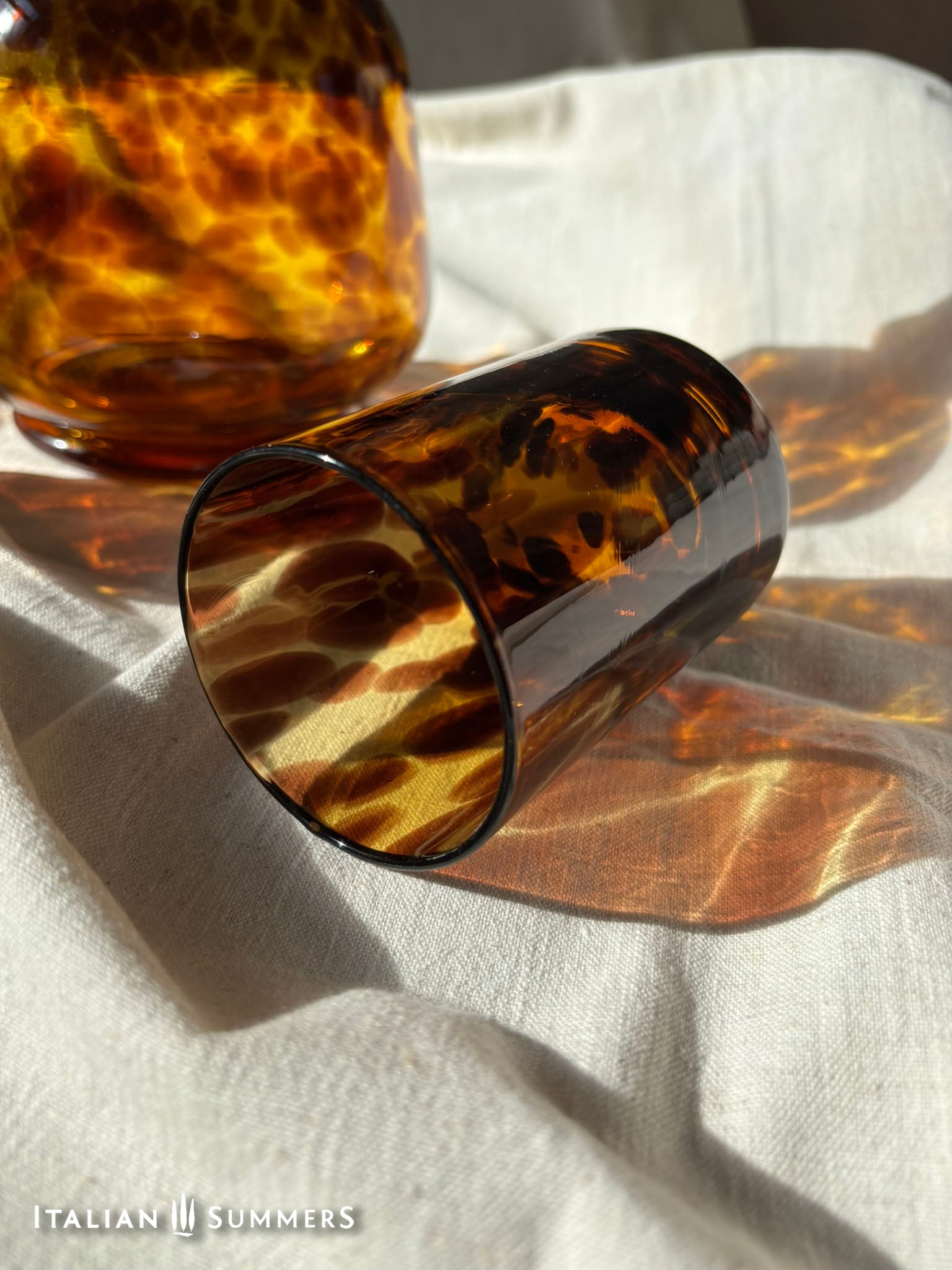 Tortoiseshell-patterned glasses on a light fabric surface with 'Italian Summers' branding.
