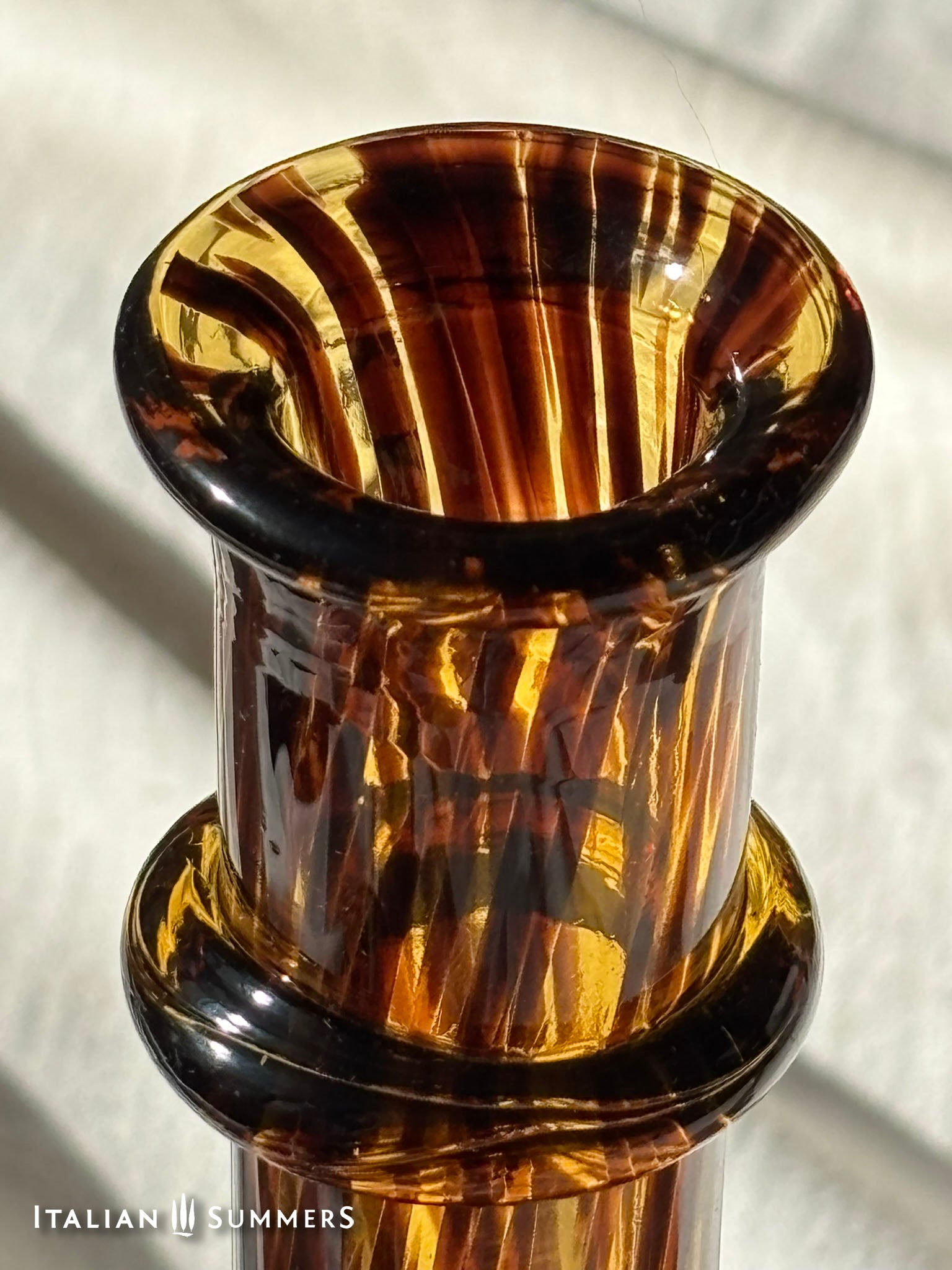 Tortoiseshell glass decanter detail on a white fabric background.